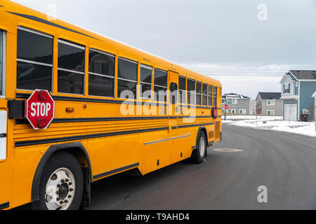 Seitenansicht eines School Bus auf einer Straße, die durch verschneite Häuser im Winter Stockfoto