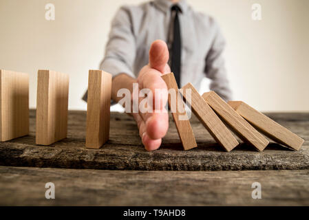 Geschäftsmann, der Domino-Effekt einfügen seine Hand zwischen fallenden und aufrechte Holzklötze in eine Nahaufnahme Konzeptbild Einhalt zu Gebieten. Stockfoto