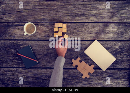 Draufsicht der Geschäftsmann Hand organisieren kleine Holzklötzchen auf rustikalen Tisch mit Noten und eine Tasse Kaffee, getönten Rückwirkung. Stockfoto