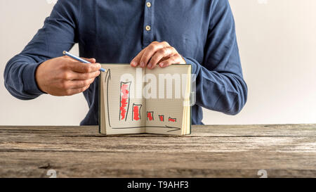 Geschäftsmann sein Notizbuch mit sinkenden finanziellen Diagramme zeigen gefärbt rot zeigen Rückgang der Gewinne und Einkommen. Stockfoto