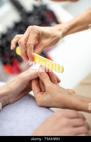 Detailansicht der Maniküre, Maniküre, feilen Fingernagel mit einer Nagelfeile mit verschiedenen Nägel poliert im Hintergrund. Stockfoto