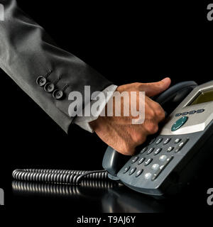 Nahaufnahme der Hand eines Geschäftsmannes abnehmen des Hörers ein schwarzes Land Telefon, platziert auf dem Schreibtisch mit textfreiraum auf schwarz Stockfoto