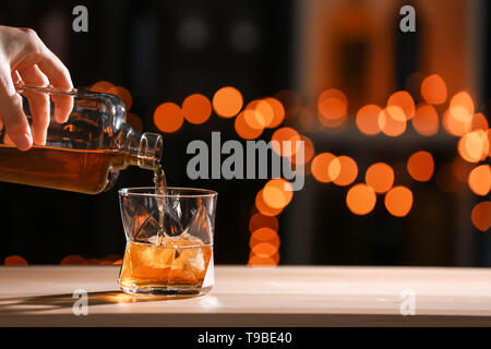 Frau giesst Whiskey aus Flasche in Glas auf hölzernen Tisch Stockfoto