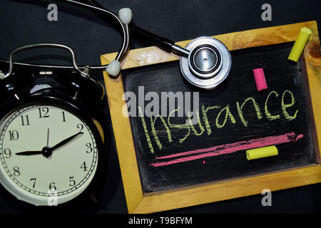 Die worte Versicherung Handschrift auf der Tafel in der Ansicht von oben. Wecker, Stethoskop auf schwarzem Hintergrund. Mit Bildung, medizinische und gesundheitliche Konzepte Stockfoto