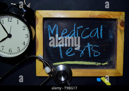 Die Worte, die medizinischen Tests Handschrift auf der Tafel in der Ansicht von oben. Wecker, Stethoskop auf schwarzem Hintergrund. Mit der Bildung, Medizin und Gesundheitswesen, Konzeption Stockfoto