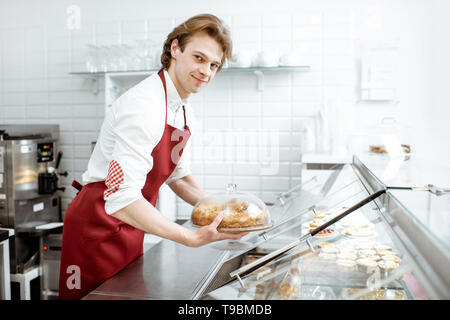 Verkäufer in rot Schürze, frischen Kuchen in den Kühlschrank des Showcase an der modernen Konditorei Stockfoto