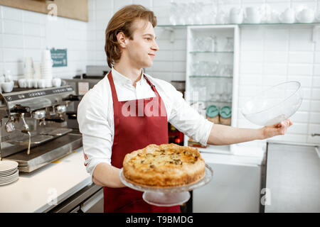 Verkäufer in rot Schürze, frischen Kuchen in den Kühlschrank des Showcase an der modernen Konditorei Stockfoto