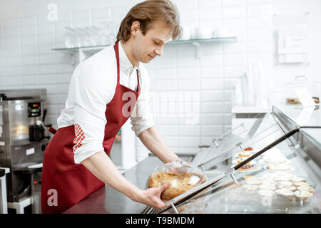 Verkäufer in rot Schürze, frischen Kuchen in den Kühlschrank des Showcase an der modernen Konditorei Stockfoto