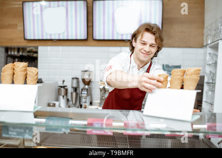 Schön lächelnden Verkäufer unter Waffel Kegel während Eis für den Client in der modernen Konditorei Stockfoto