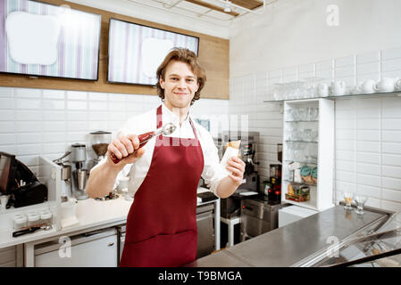 Lustige Portrait eines Eis Verkäufer in rot Schürze mit Waffel Kegel in der Konditorei Stockfoto