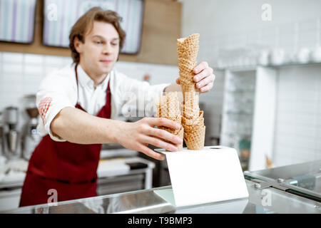 Stattliche Verkäufer unter Waffel Kegel während Eis für den Client in der modernen Konditorei Stockfoto