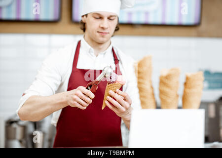 Junge Verkäufer in Schürze und Mütze, Eis mit Waffel Konus an der modernen Konditorei Stockfoto