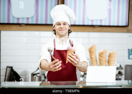 Porträt einer stattlichen Verkäufer in rot Schürze und hat den Verkauf von Eis in der modernen Konditorei Stockfoto
