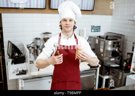 Porträt einer stattlichen Verkäufer in rot Schürze und hat den Verkauf von Eis in der modernen Konditorei Stockfoto