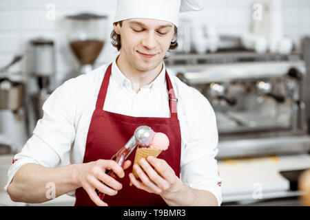 Junge Verkäufer in Schürze und Mütze, Eis mit Waffel Konus an der modernen Konditorei Stockfoto