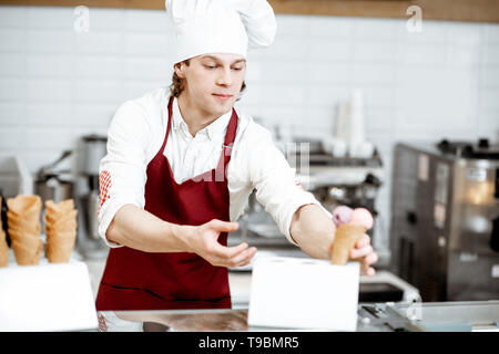 Junge Küchenchef Koch oder Verkäufer in Schürze und hat den Verkauf von Eis in der Waffel Kegel in der modernen Konditorei Stockfoto