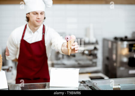 Junge Küchenchef Koch oder Verkäufer in Schürze und hat den Verkauf von Eis in der Waffel Kegel in der modernen Konditorei Stockfoto
