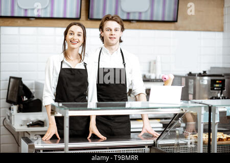 Porträt eines Mannes und einer Frau im schwarzen Schürzen zusammen als Verkäufer in der modernen Konditorei und Café Stockfoto