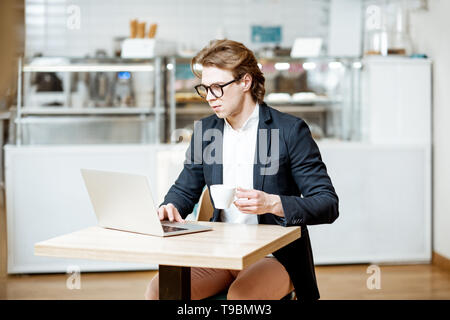 Junge Unternehmer arbeiten mit Laptop, während in der modernen Cafe oder Konditorei sitzen Stockfoto