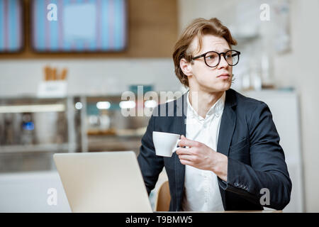 Junge Unternehmer arbeiten mit Laptop, während in der modernen Cafe oder Konditorei sitzen Stockfoto