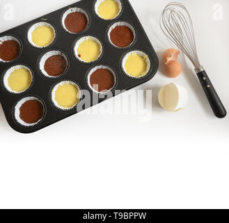 Muffin Backblech mit hellen und dunklen Kuchen Teig für Muffins, Schneebesen, Eierschale und Pappbecher gefüllt, Hintergrund verblasst zu weiss, große Kopie Raum, h Stockfoto