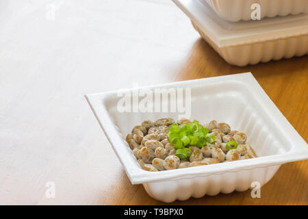 Natto - eine beliebte und gesunde Japanische Lebensmittel aus vergorenem Bohnen in einem Styropor Behälter mit grünen Frühlingszwiebeln als Belag. Stockfoto