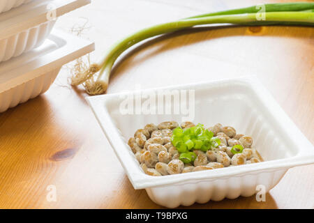 Natto - eine beliebte und gesunde Japanische Lebensmittel aus vergorenem Bohnen in einem Styropor Behälter mit grünen Frühlingszwiebeln als Belag. Stockfoto