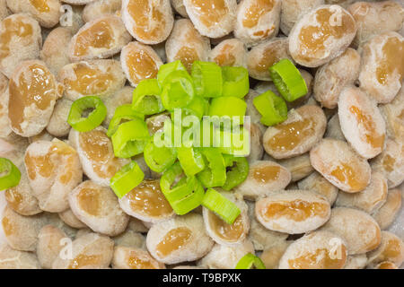 Natto - eine beliebte und gesunde Japanische Lebensmittel aus vergorenem Bohnen in einem Styropor Behälter mit grünen Frühlingszwiebeln als Belag. Stockfoto