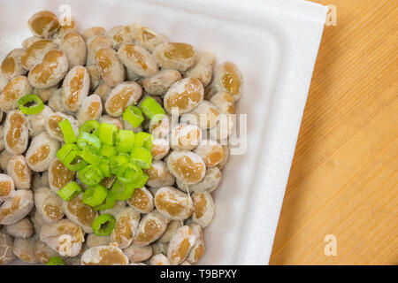 Natto - eine beliebte und gesunde Japanische Lebensmittel aus vergorenem Bohnen in einem Styropor Behälter mit grünen Frühlingszwiebeln als Belag. Stockfoto