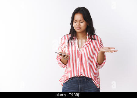 Wtf soll es bedeuten. Portrait von verwirrten und frustrierten jungen Freundin ständigen befragt zuckend und runzelte die Stirn, als Holding Smartphone lesen Stockfoto