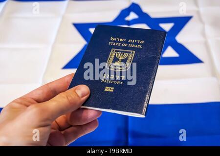 Hand, die den Pass des Staates Israel, israelische Flagge im Hintergrund. Israel die israelische Staatsbürgerschaft Konzept, biometrische "arkon 'Pass Stockfoto