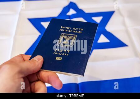 Hand, die den Pass des Staates Israel, israelische Flagge im Hintergrund. Israel die israelische Staatsbürgerschaft Konzept, biometrische "arkon 'Pass Stockfoto