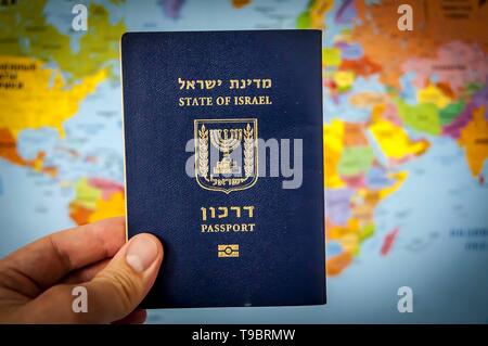 Hand, die den Pass des Staates Israel gegen die bunte Welt Karte Atlas. Israel die israelische Staatsbürgerschaft Konzept, biometrische "arkon 'Pass Stockfoto