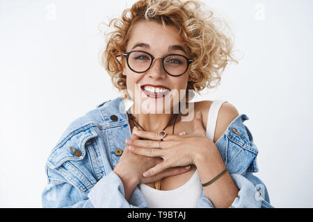 Nahaufnahme der froh und dankbar beeindruckt sehr charmante Frau mit blonden kurzen curly Haarschnitt holding Palmen auf der Brust dankbar und lächelnd Stockfoto