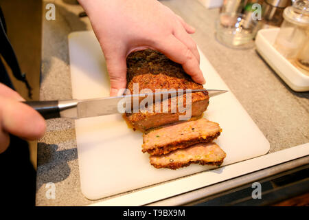 Frau Hände schneiden Stück Hackbraten, sie für die Verkostung der Lebensmittel in der Küche zubereiten. Koch schneiden Hackbraten mit Messer an Bord Restaurant Küche. Stockfoto