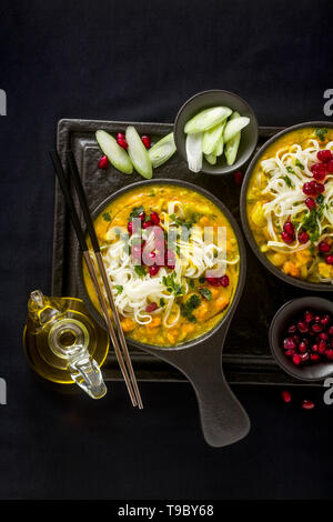 Laksa mit Kürbis und Kokosmilch, Reisnudeln, Brokkoli und Granatapfel Samen portioniert in die schwarzen Platten auf einem dunklen Hintergrund. gesund vegan Gericht Stockfoto