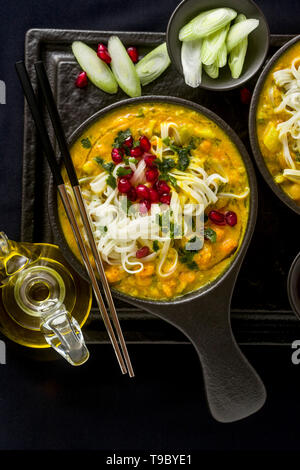 Laksa mit Kürbis und Kokosmilch, Reisnudeln, Brokkoli und Granatapfel Samen portioniert in die schwarzen Platten auf einem dunklen Hintergrund. gesund vegan Gericht Stockfoto