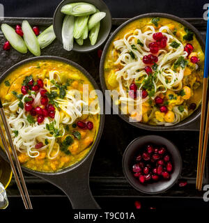 Laksa mit Kürbis und Kokosmilch, Reisnudeln, Brokkoli und Granatapfel Samen portioniert in die schwarzen Platten auf einem dunklen Hintergrund. gesund vegan Gericht Stockfoto