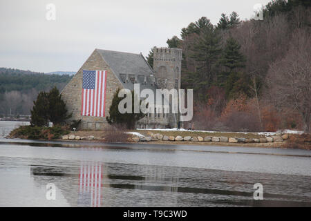 Alte Steinkirche am Rand des Wachusett Stausees mit großen amerikanische Flagge hängt an der Seite mit Schnee noch auf Boden im Mai Stockfoto