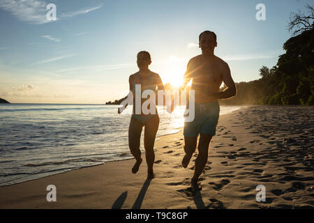 Sun Flare über die Silhouette eines jungen Paares halten einander die Hände Laufen am Strand Stockfoto