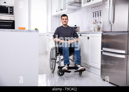 Lächelnden jungen Behinderten Mann sitzt im Rollstuhl In der Küche Stockfoto