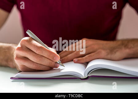 Hand eines Mannes schreiben etwas auf einem sauberen Notebook oben auf dem Tisch hautnah. Stockfoto