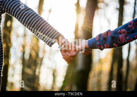 Niedrigen Winkel Blick auf zwei Freundinnen oder Partner holding Pinkies mit Hintergrund unscharf Bäume und strahlendem Sonnenschein. Stockfoto