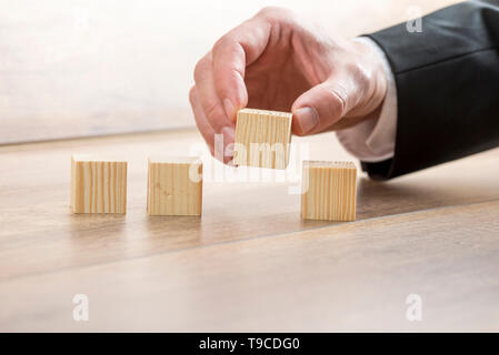 Nahaufnahme der männlichen Hand in eleganten Anzug platzieren vier leere Holzwürfel in einer Reihe. Stockfoto