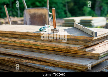 Hammer, Handschuhe und Bauherren Ebene auf einem Haufen von Holzbohlen in eine Terrasse mit Blick auf den Garten in eine Konstruktion und den Bau von Konz zu schützen Stockfoto