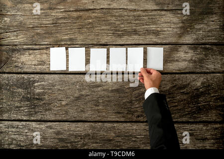 Top view of male hand placing six empty white cards in a row over a textured rustic wooden desk. Stockfoto