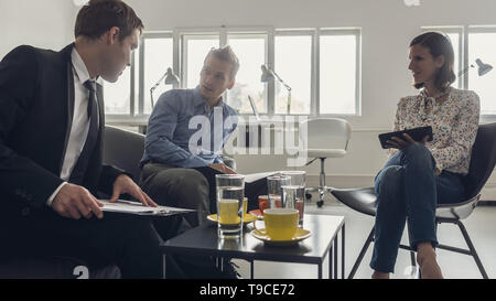 Drei Personen sitzen um einen Tisch in einem Büro in einer Sitzung. Stockfoto