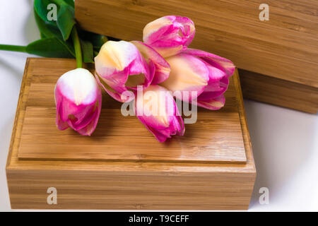 Ein Strauß Blumen auf weißem Hintergrund mit Holz- Krusten. Lila Tulpen liegen auf einer Holzkiste. Blume Geschenk Konzept. Für Ihren Text. Minimale co Stockfoto