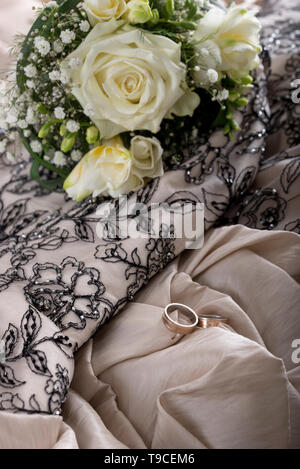 Hochzeit-Einstellung mit schöne Braut Strauß Blumen und zwei Trauringe liegen auf einer goldenen Hochzeitskleid. Stockfoto