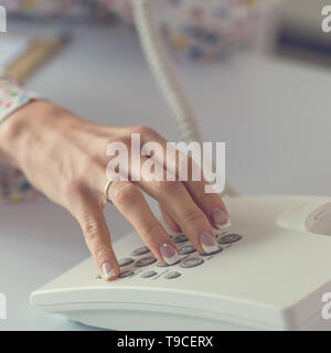 Detailansicht der weiblichen Hand Wählen einer Telefonnummer mit weißen Festnetztelefon. Stockfoto